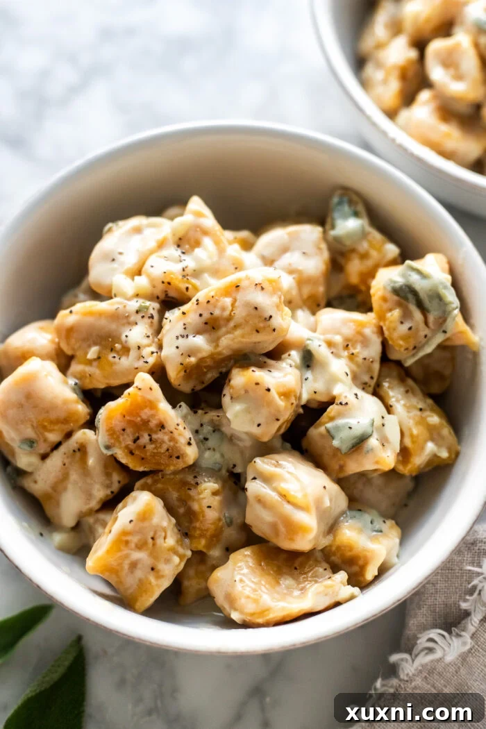 A serving bowl filled with golden vegan pumpkin gnocchi, drizzled with a rich brown butter sage sauce and fresh herbs.
