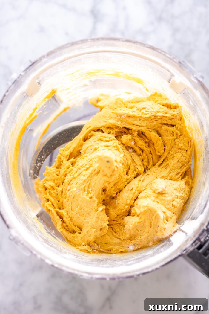 Pumpkin gnocchi dough being formed in a food processor, showcasing its cohesive texture.