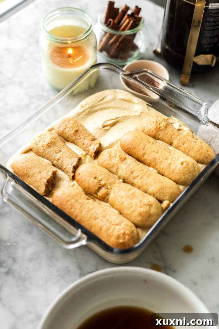 Initial steps of assembling the vegan pumpkin tiramisu, showing ladyfingers being carefully dipped in espresso and precisely placed in the casserole dish.