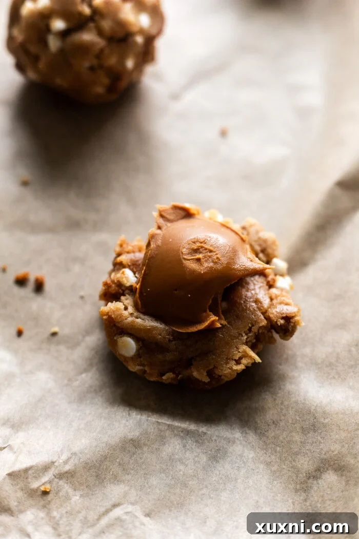 Hands stuffing a frozen dollop of Biscoff cookie butter into cookie dough.
