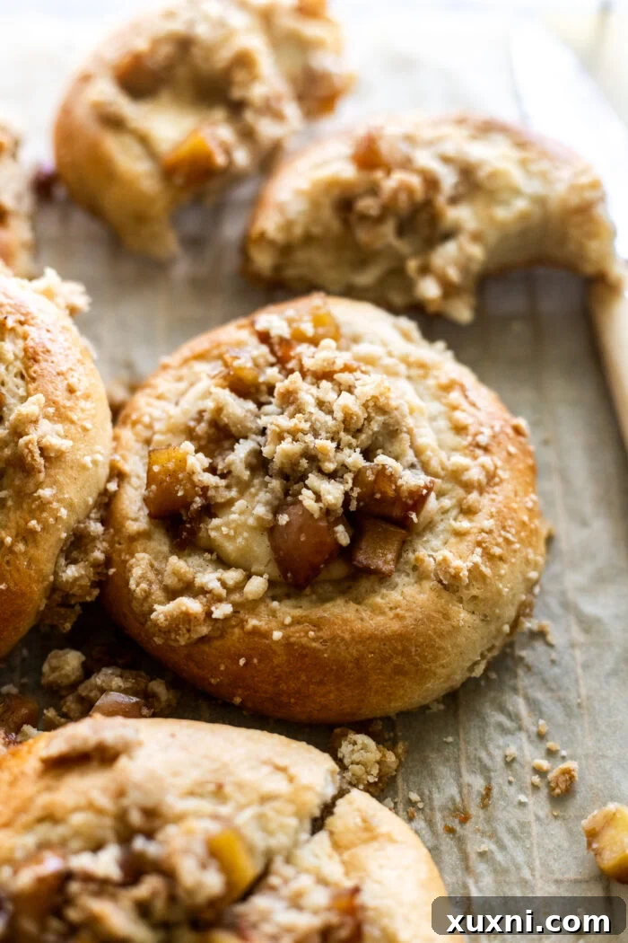 Pillowy soft vegan apple cheesecake brioche buns on parchment paper, fresh from the oven, showcasing their golden crust and enticing crumble topping.