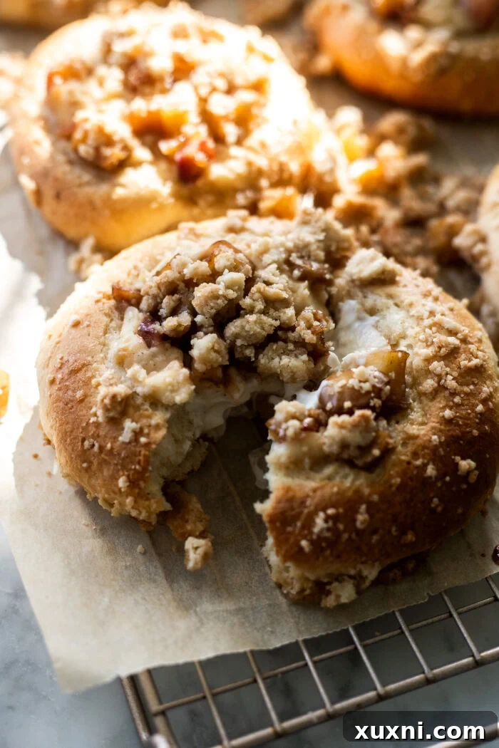 A broken open vegan apple cheesecake brioche bun on parchment paper, revealing its lush dairy-free cheesecake filling and cinnamon-spiced apple chunks.