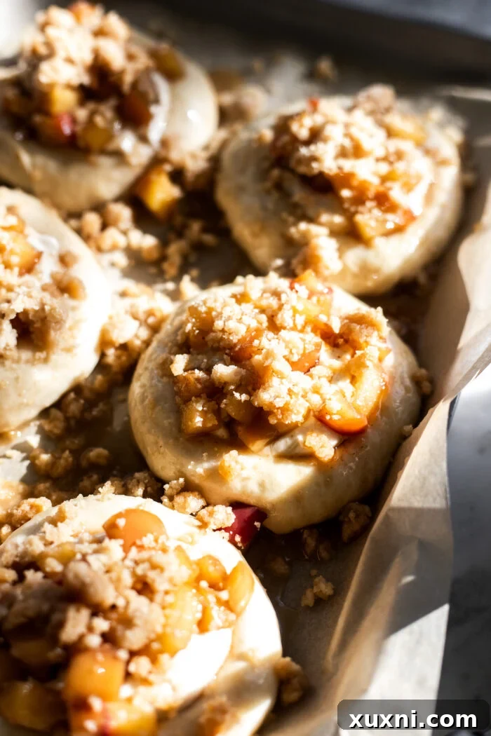 Unbaked brioche buns with indentations, waiting for their cheesecake and apple fillings before the final proof and baking.