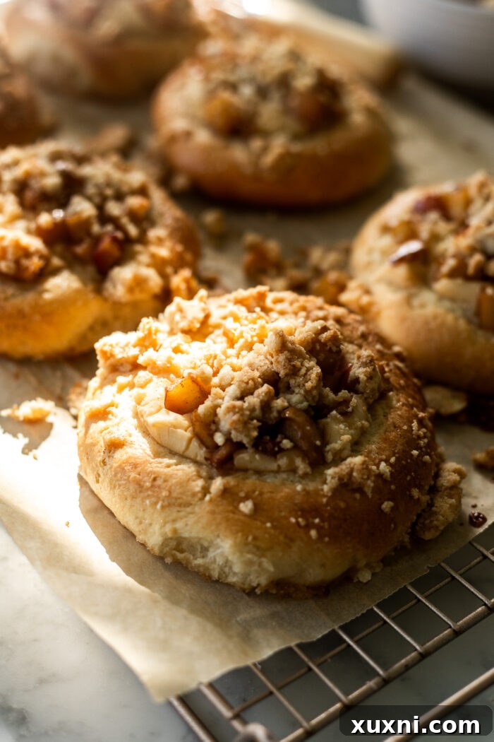 A tray of beautifully baked vegan apple cheesecake brioche buns, golden brown and topped with crumble, cooling on a rack.
