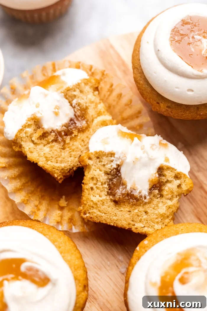 A vegan salted caramel cupcake sliced open to reveal a rich, gooey caramel center, topped with a swirl of dairy-free cream cheese frosting and a drizzle of caramel.
