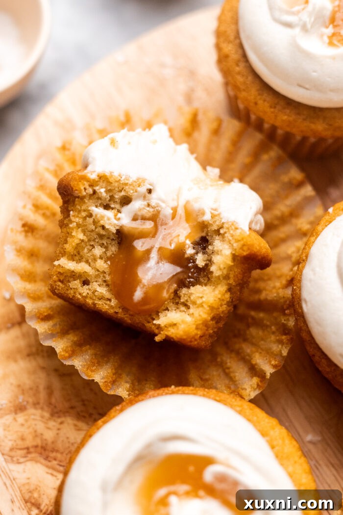A close-up of a perfectly baked and frosted vegan caramel cupcake with a bite taken, highlighting its soft texture and inviting filling.