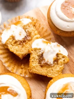 A vegan salted caramel cupcake sliced open to reveal a rich, gooey caramel center, topped with a swirl of dairy-free cream cheese frosting and a drizzle of caramel.