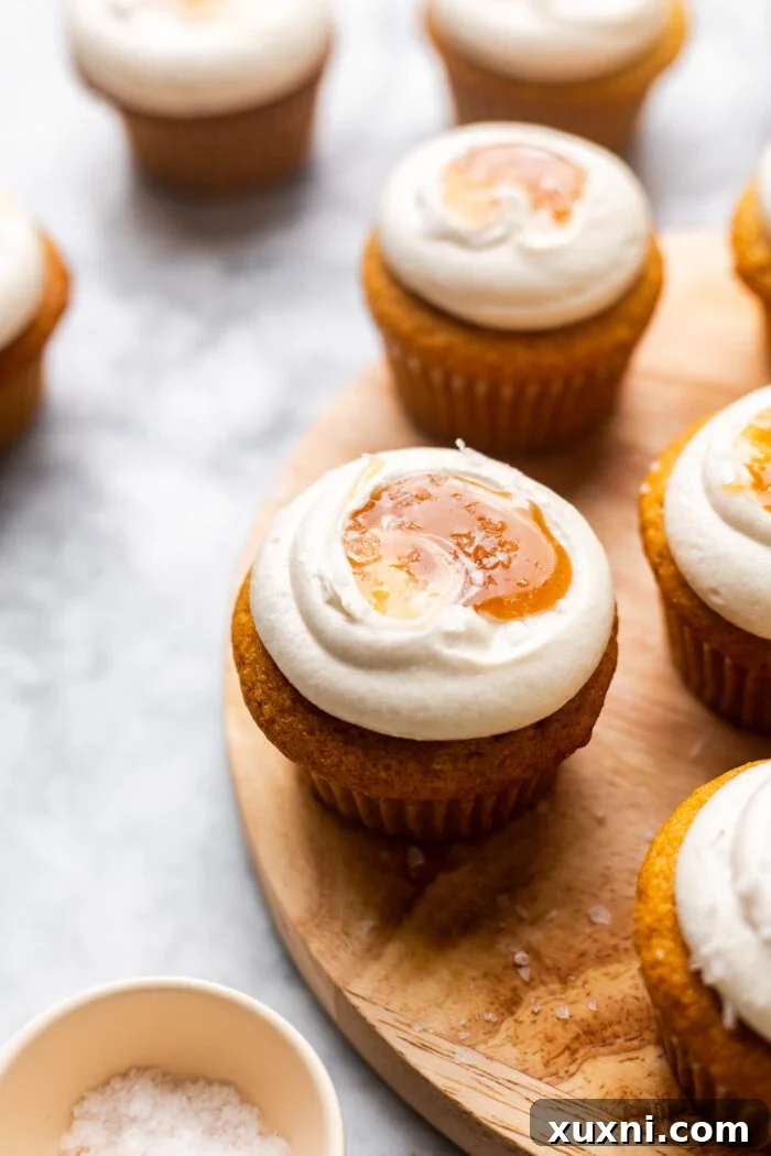 Beautifully arranged salted caramel cupcakes on a rustic wooden board, set against a elegant marble table backdrop, showcasing their perfect frosting swirls and caramel drizzles.