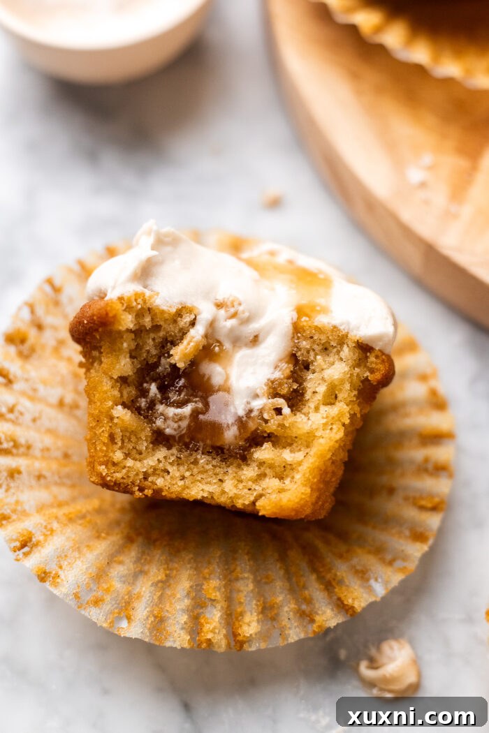A close-up shot of a vegan caramel cupcake, with a bite taken out, showing the moist cake, gooey caramel filling, and fluffy cream cheese frosting.