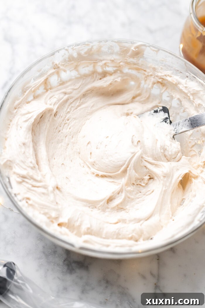A piping bag filled with creamy vegan caramel cream cheese frosting, ready to top the prepared cupcakes.