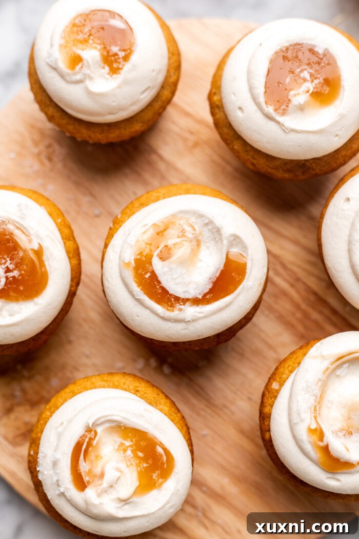 A pair of exquisitely frosted vegan caramel cupcakes, featuring a generous swirl of cream cheese frosting and a glistening caramel topping.