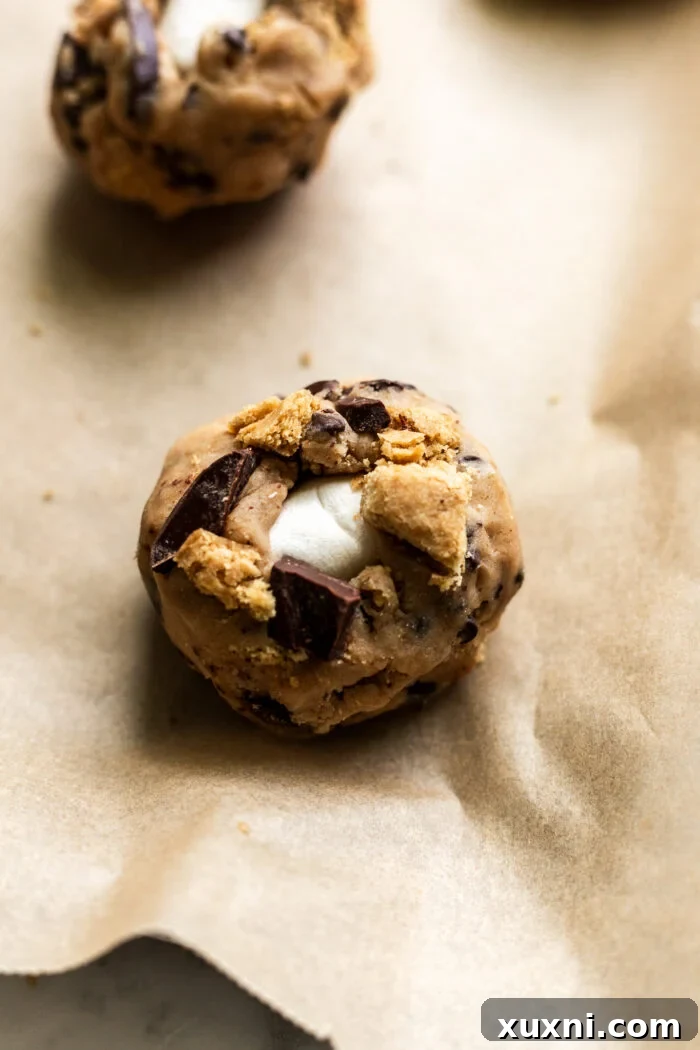 Raw vegan s'mores cookie dough balls with visible marshmallow centers, ready for the oven.