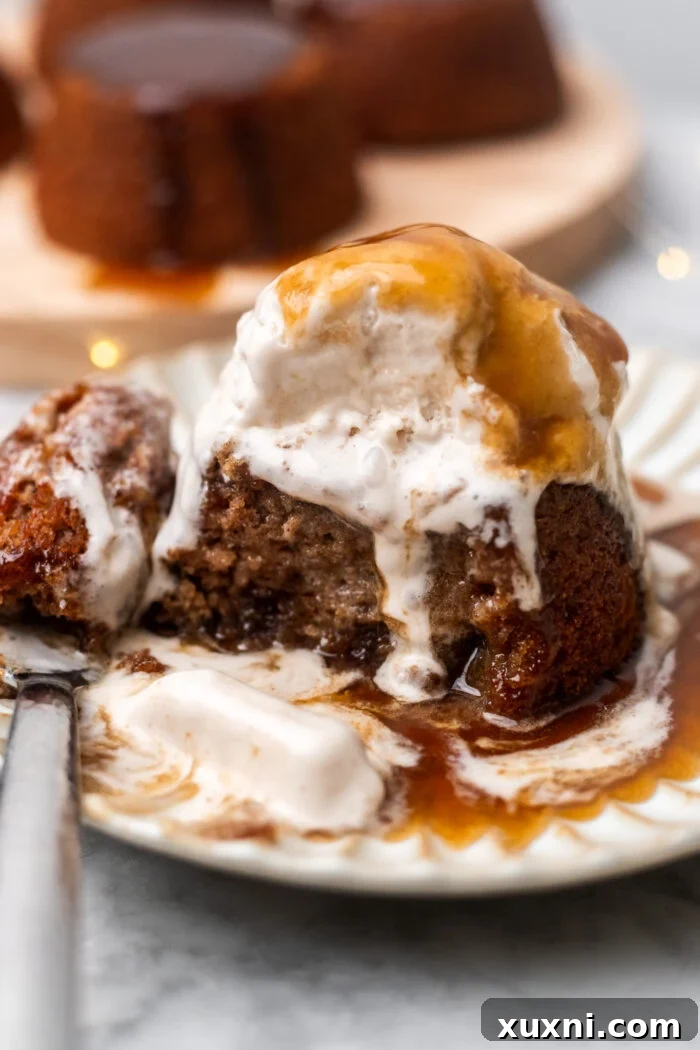 Decadent sticky toffee pudding, perfectly moist, served with creamy vegan vanilla ice cream and drizzled with luscious toffee sauce on a white plate