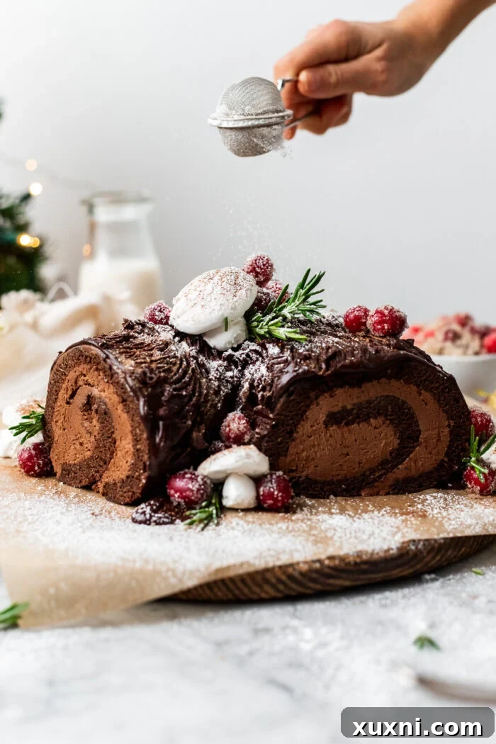 Beautifully decorated Vegan Christmas Yule Log Cake (Bûche De Noël) with a hand gently sprinkling powdered sugar, highlighting its rustic charm and festive appeal.