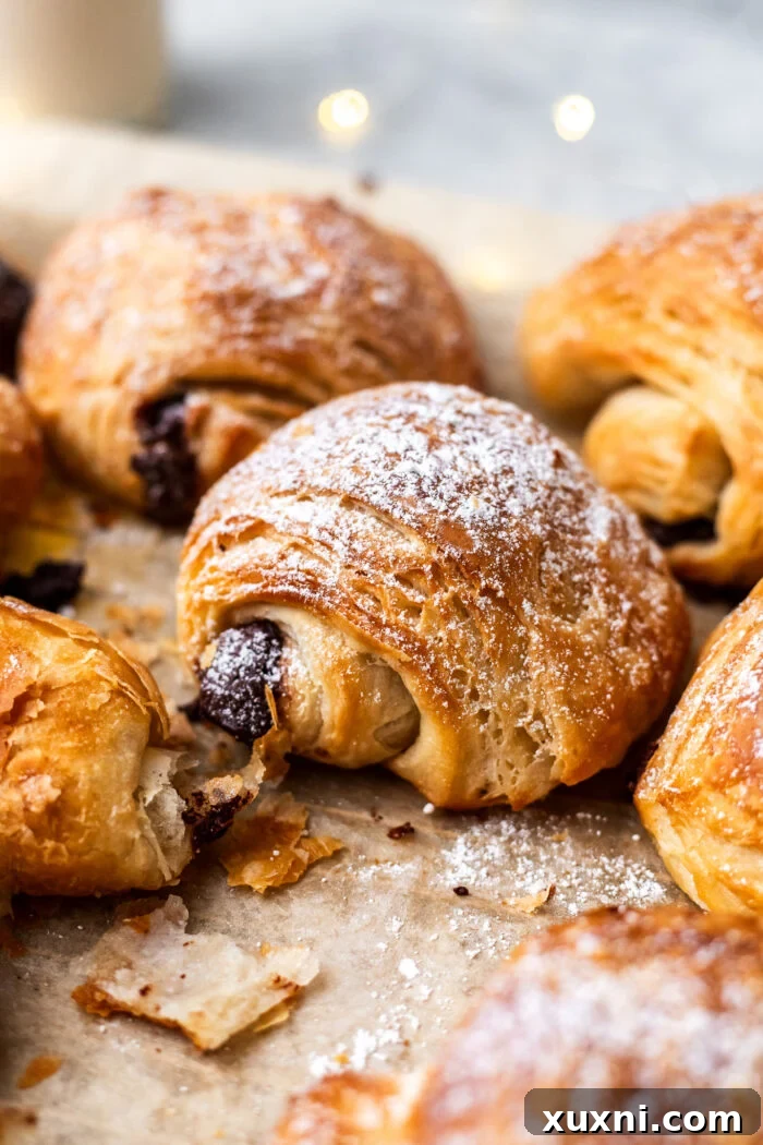 Beautifully baked vegan pain au chocolat on parchment paper, showcasing their golden-brown, flaky exterior and the enticing hint of melted chocolate.