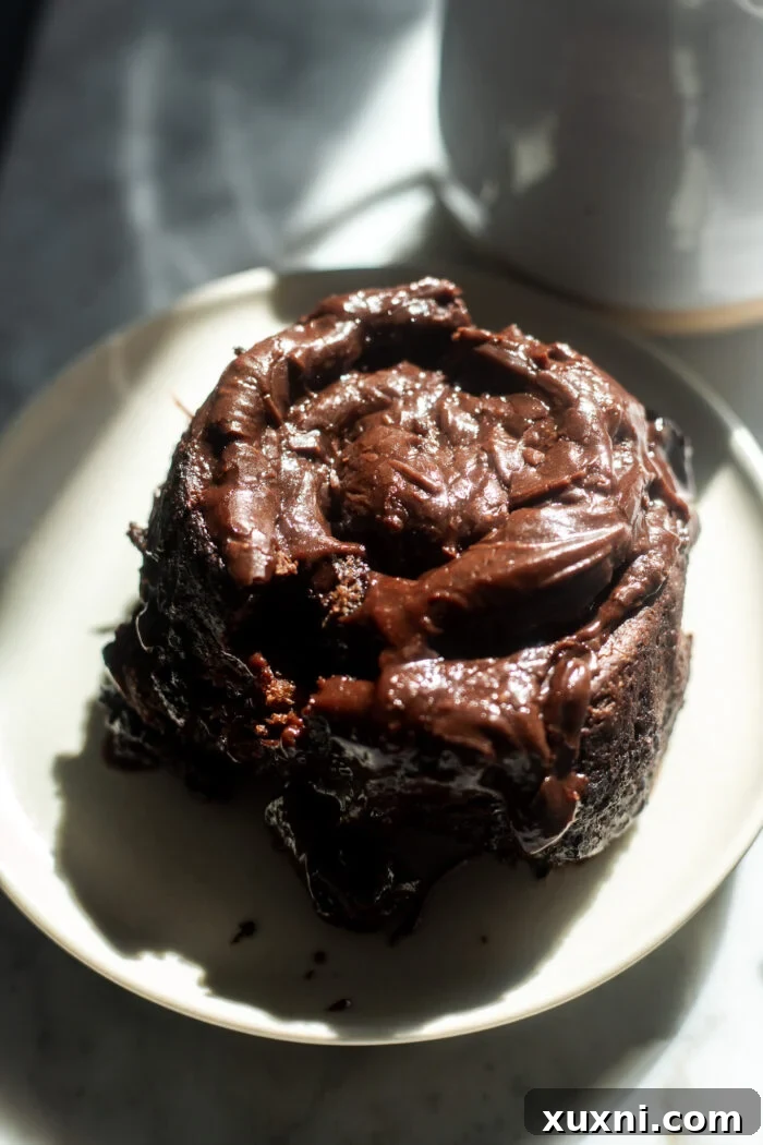 A single vegan chocolate cinnamon roll cut in half on a plate, showing its rich, gooey chocolate swirl and fluffy interior.