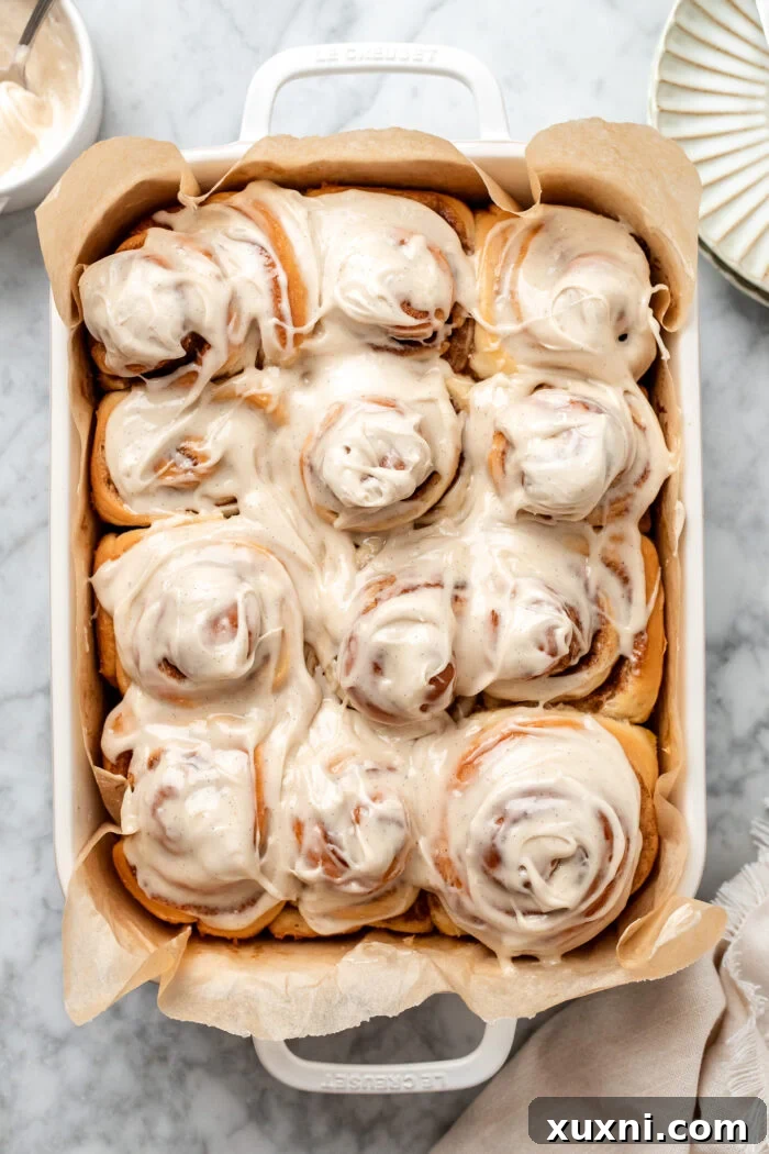 Gooey vegan cinnamon rolls fresh out of the oven in a casserole dish, topped with generous icing.