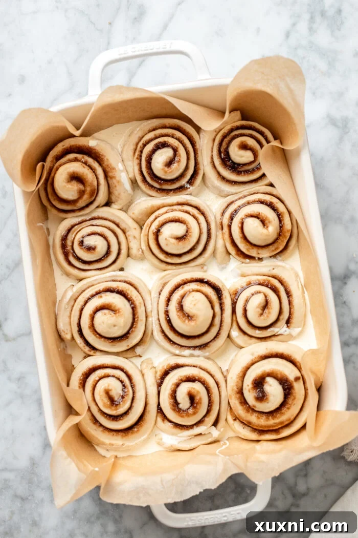 Vegan cinnamon rolls in a baking dish with vegan heavy cream poured between them before baking.