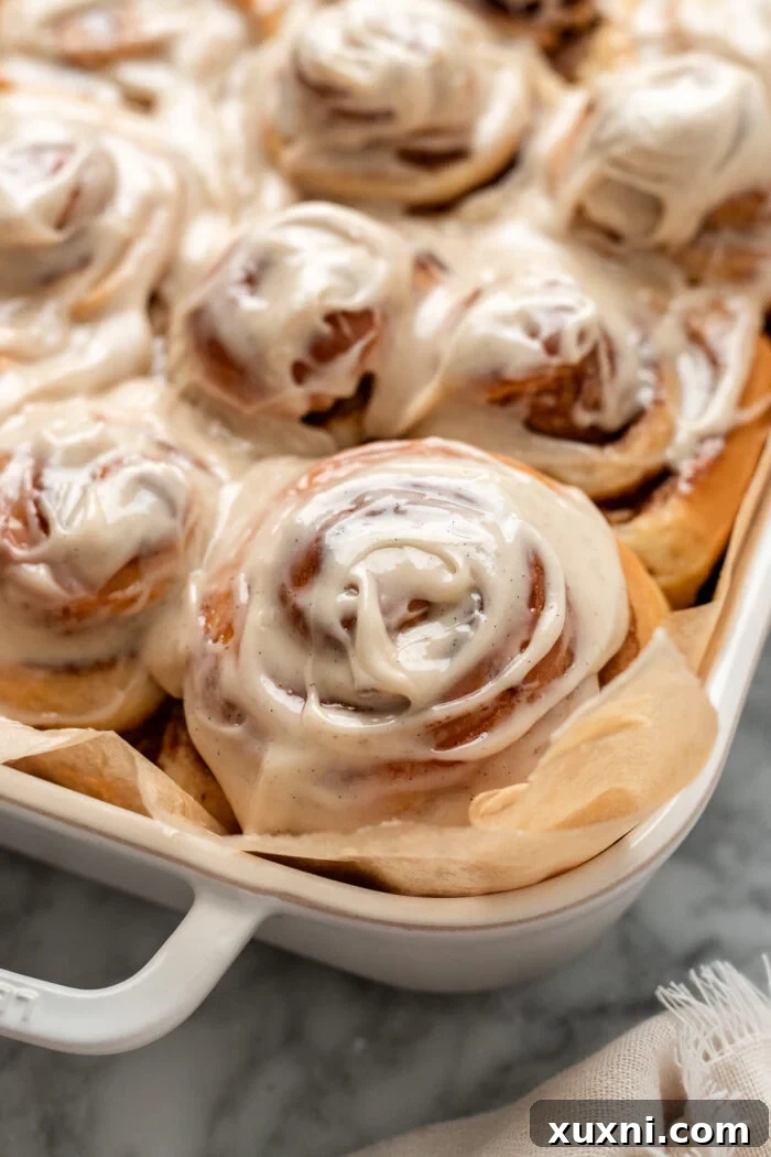 A close-up shot of baked vegan cinnamon rolls in a white casserole dish, glistening with melted icing.