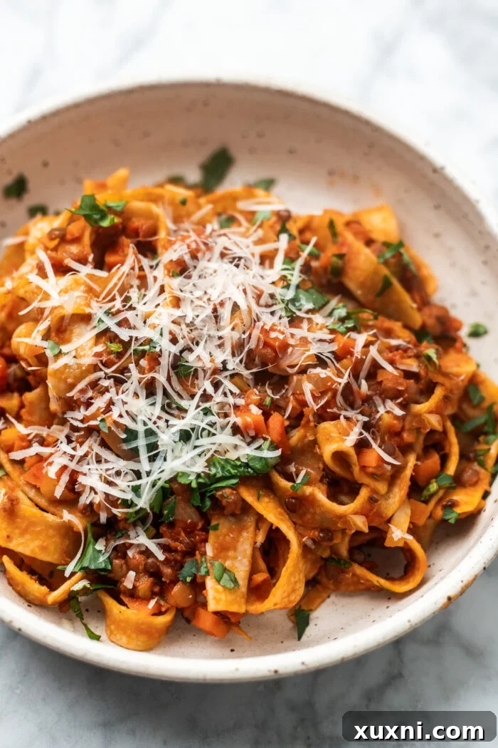 The Easiest 8-Ingredient Plant-Based Bolognese 2 Perfect bowl of lentil bolognese with grated vegan parmesan and fresh herbs on top, showcasing a delicious plant-based meal.