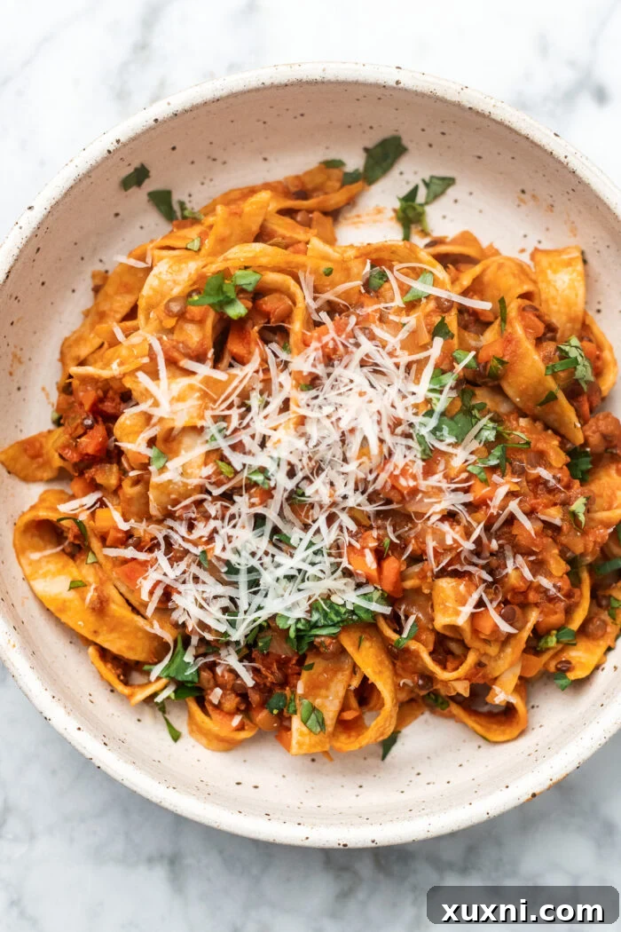 The Easiest 8-Ingredient Plant-Based Bolognese 3 A vibrant bowl of lentil bolognese served with tagliatelle pasta, garnished with vegan cheese and chopped fresh herbs.