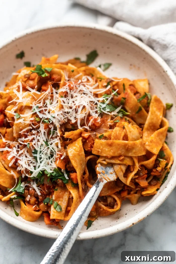 The Easiest 8-Ingredient Plant-Based Bolognese 4 Close-up shot of a bowl of rich lentil bolognese with a fork twirled in pasta, showcasing its hearty texture and appetizing appeal.