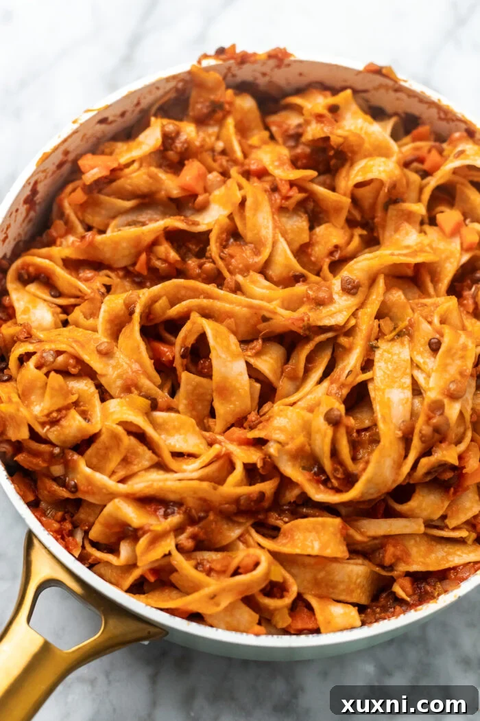 The Easiest 8-Ingredient Plant-Based Bolognese 7 Cooked spaghetti being tossed with the rich, hearty lentil bolognese sauce in a large pan.