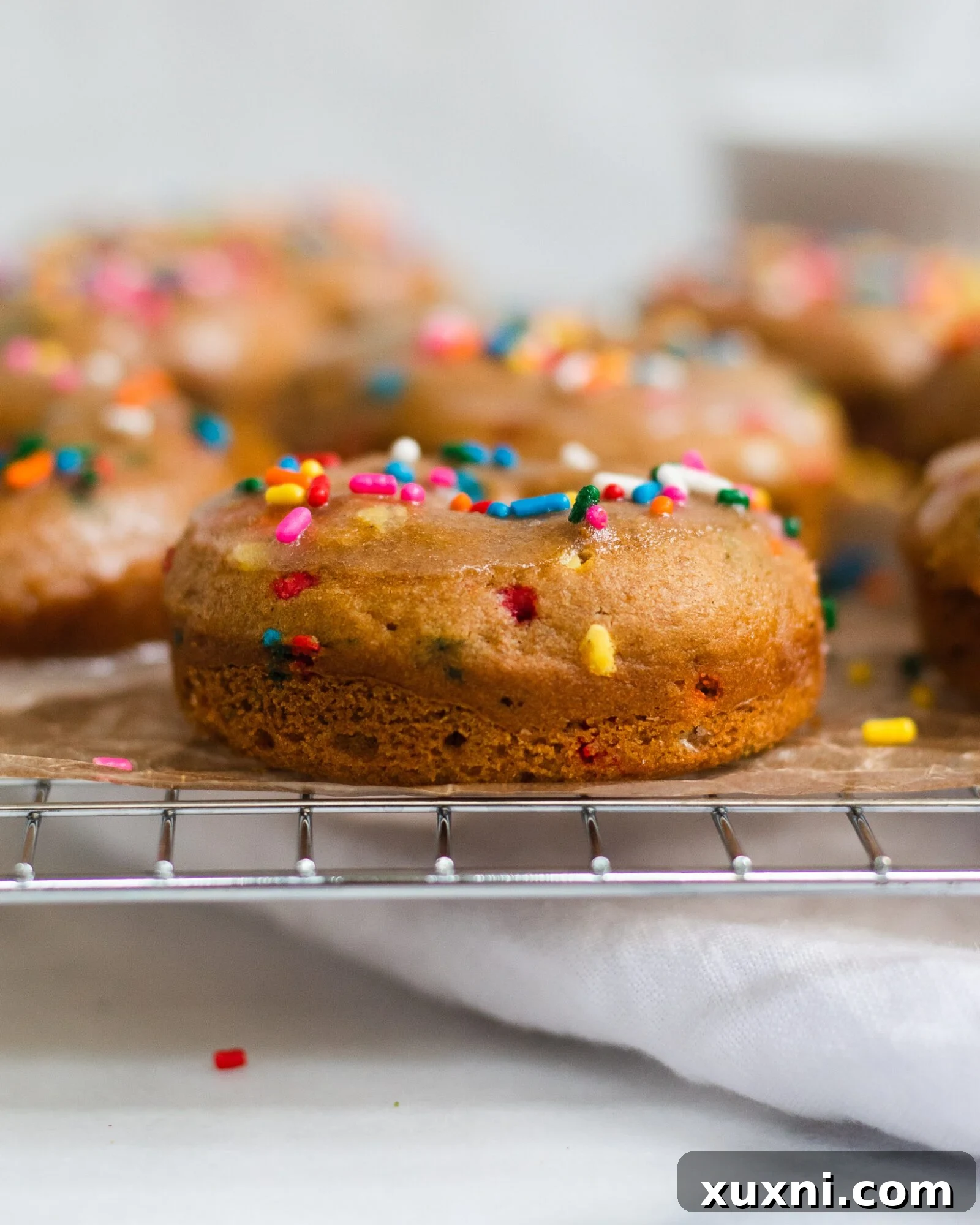 Vegan Birthday Donut Delights 17 glazed vanilla cake donut on cooling rack with sprinkles