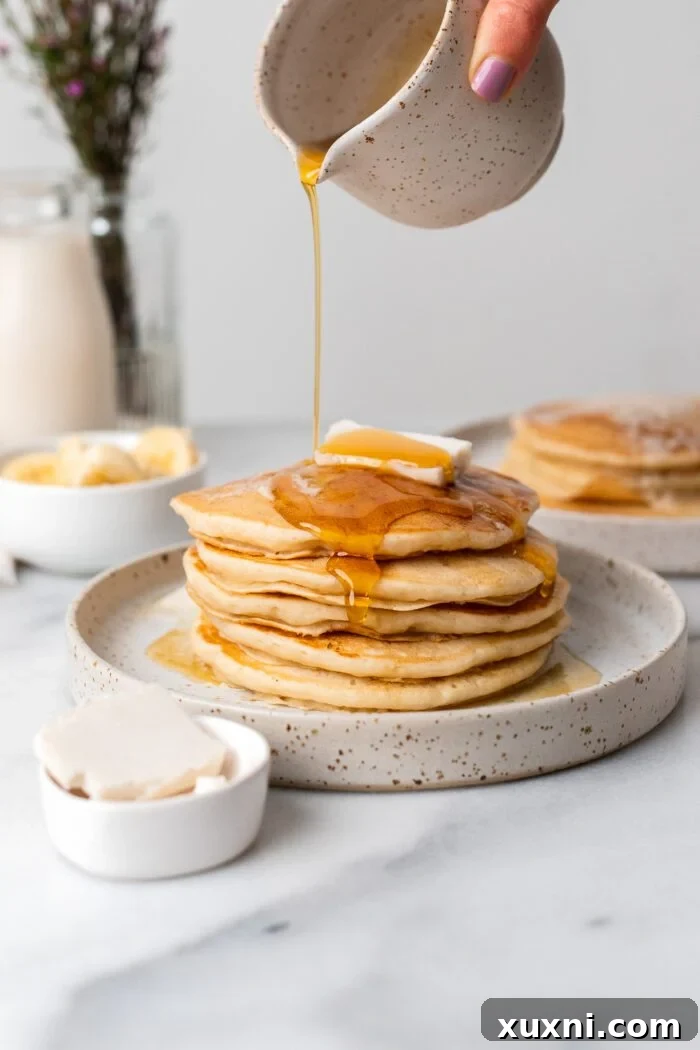Golden maple syrup being generously poured over a stack of warm vegan pancakes