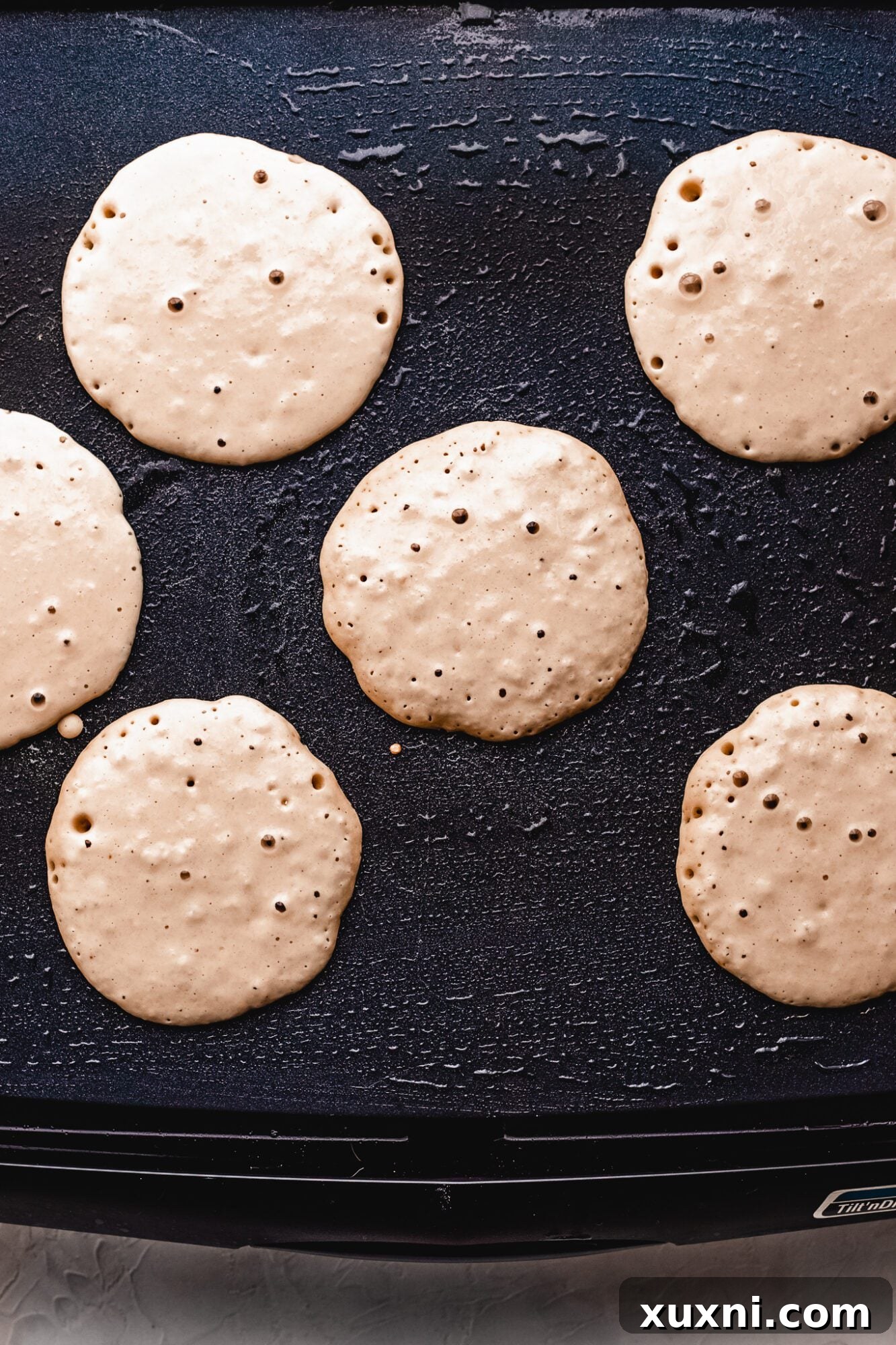 Several vegan pancakes cooking on a griddle, showing golden brown edges