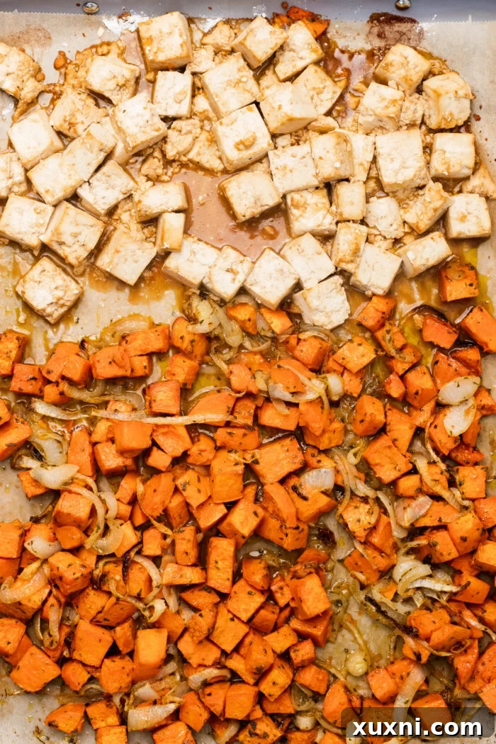 A sheet pan loaded with perfectly roasted tofu cubes and sweet potato chunks, ready for serving.