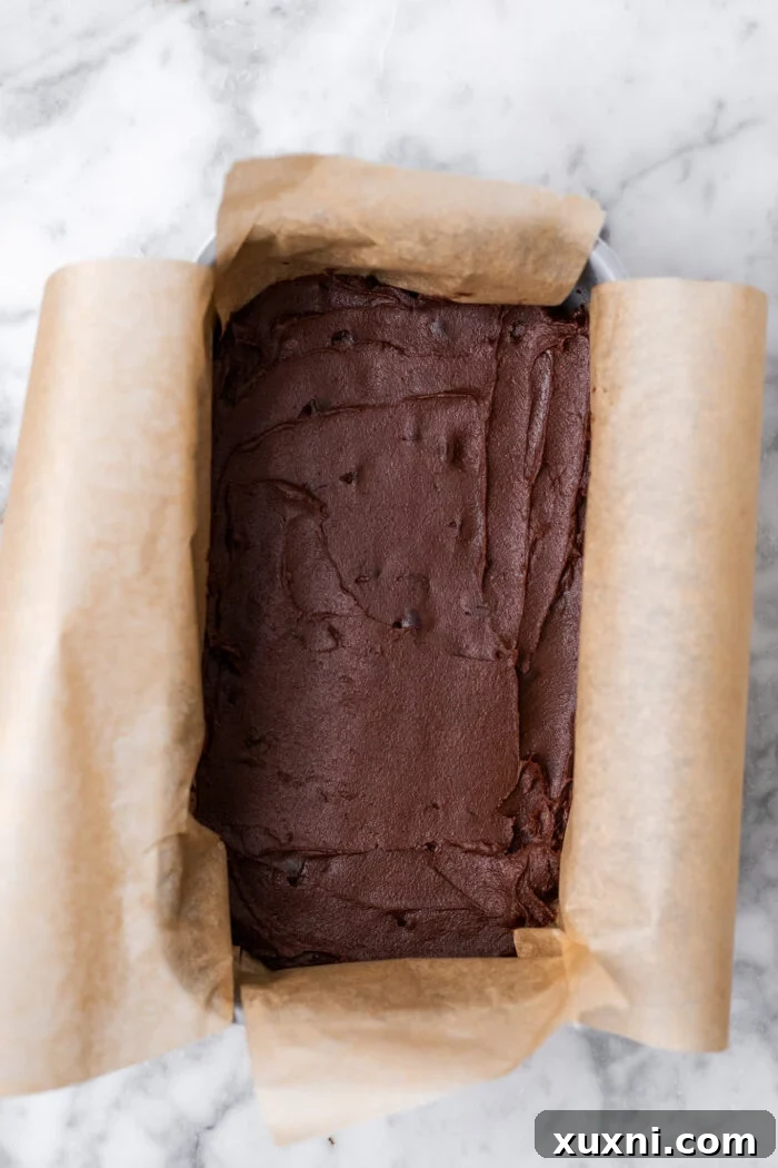 The fudgy vegan brownie base spread evenly in a loaf pan, ready for the next layer.