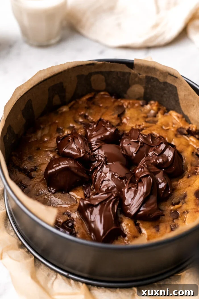 Image illustrating how to add spoonfuls of vegan Nutella onto the first layer of cookie dough in the pan.