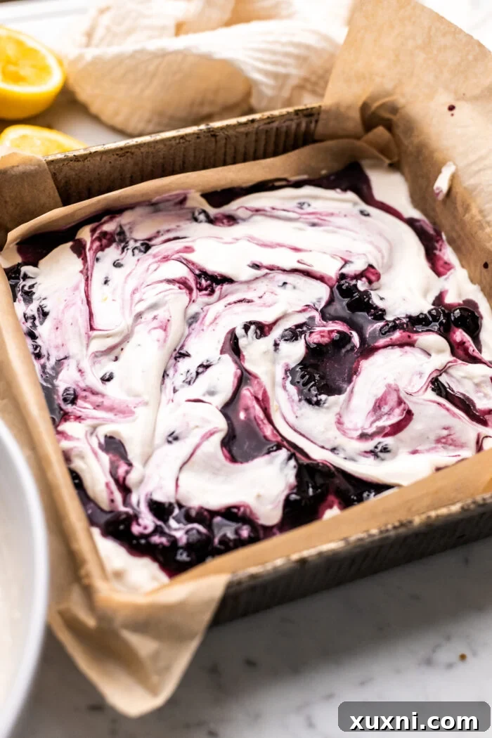 A square pan showing the first layers of graham crackers, lemon whipped cream, and blueberry sauce.