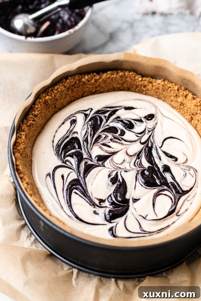 The first layer of creamy cheesecake batter in the pan, with dollops of rich fudge ripple sauce scattered on top.