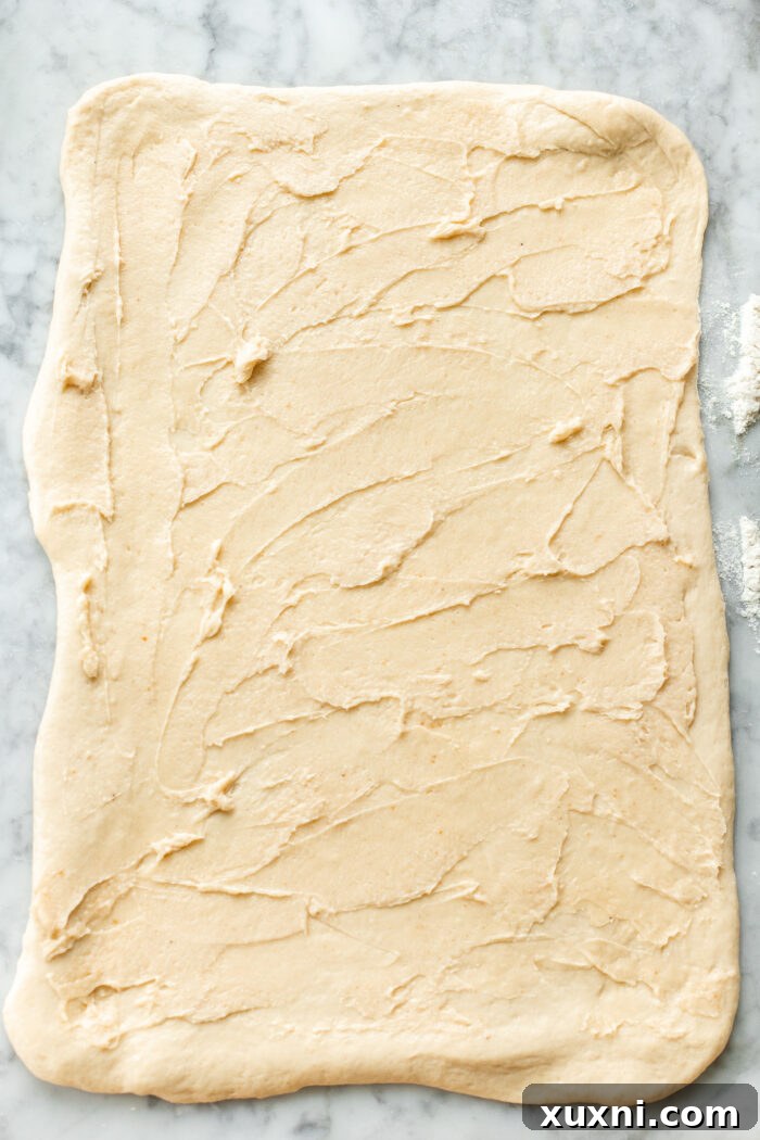 Rolled-out cinnamon roll dough, evenly spread with the maple brown butter mixture, ready for the cinnamon sugar.