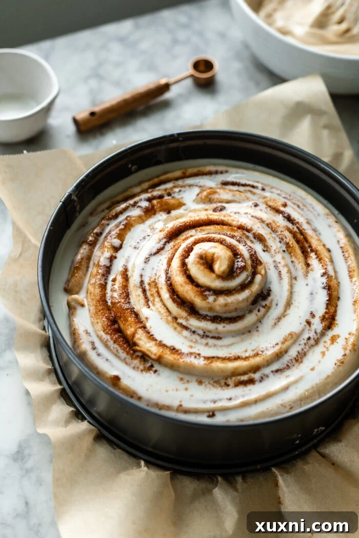 The giant cinnamon roll cake in the baking pan, after its second rise and drizzled with vegan heavy cream, ready for the oven.