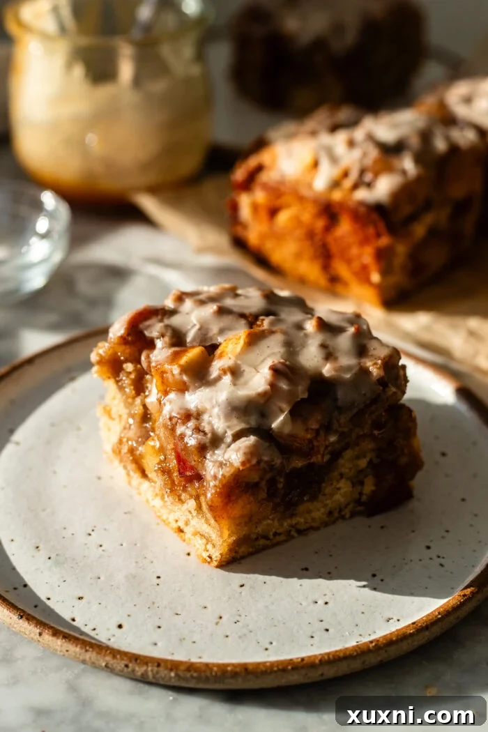 A perfectly sliced piece of vegan apple fritter cake on a white plate, showcasing its moist texture, cinnamon swirls, and tender apple chunks.
