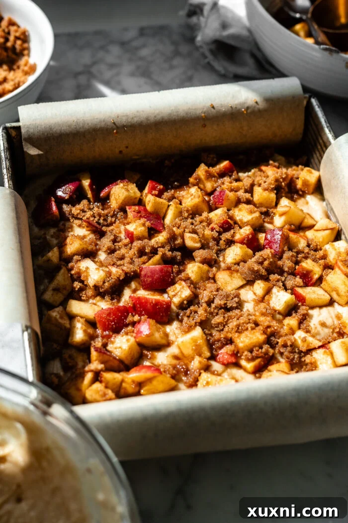 A baking pan with the first layer of vegan apple fritter cake batter, topped with spiced apple chunks and a sprinkling of cinnamon crumble.
