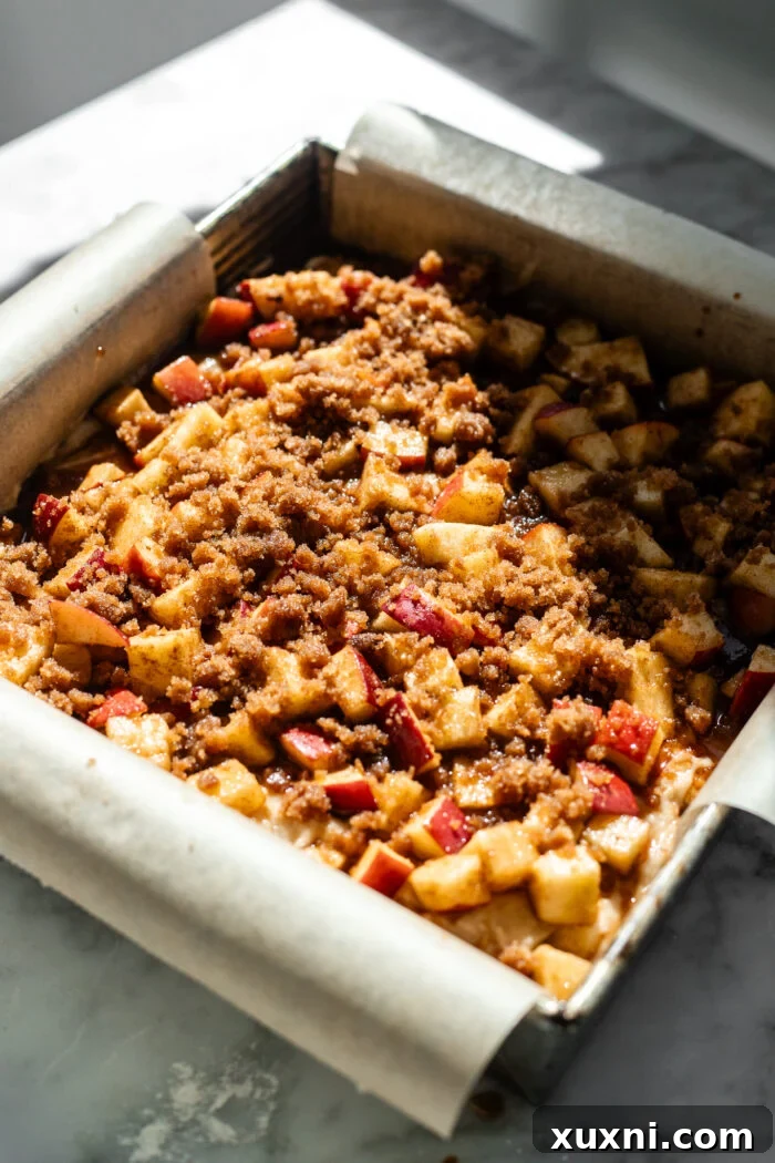 The assembled vegan apple fritter cake in a baking pan, with the final layers of batter, apples, and cinnamon crumble clearly visible on top.