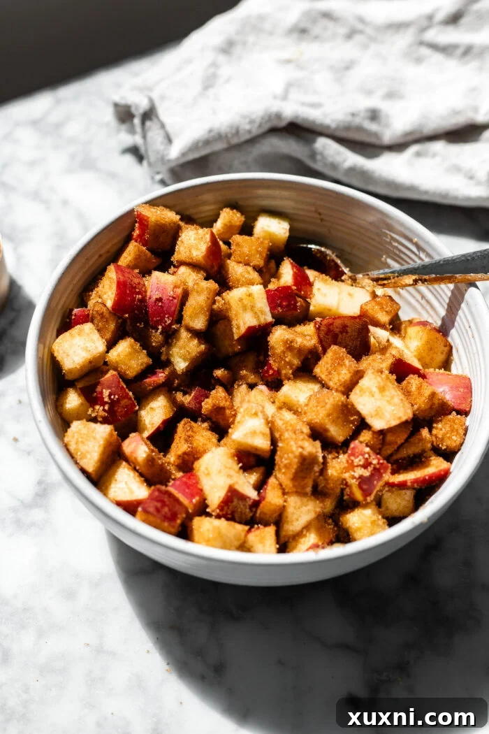 Diced apples mixed with brown sugar and cinnamon in a large bowl, ready for the maceration process.