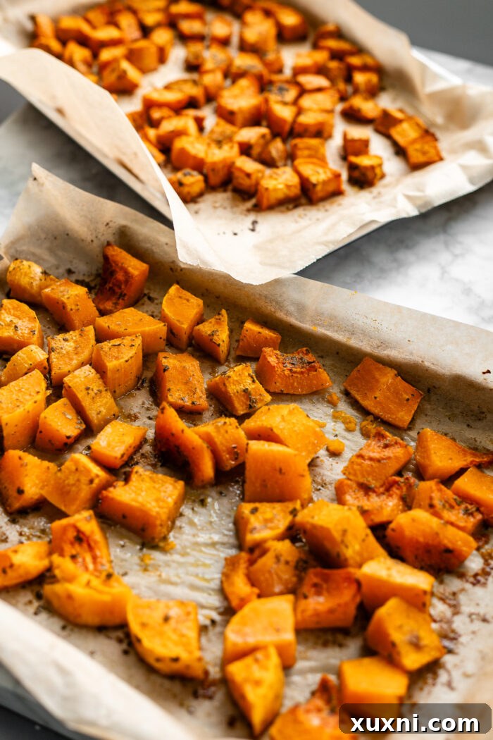 Roasted butternut squash and sweet potato cubes, with a golden-brown caramelization, on a baking sheet after cooking.