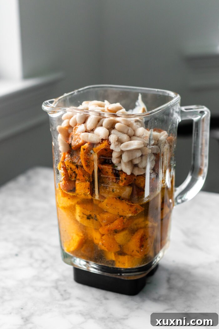 Roasted vegetables, vegetable broth, and cannellini beans placed into a high-speed blender, ready for blending.