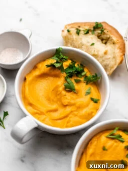 Two bowls of creamy vegan butternut squash and sweet potato soup with fresh parsley garnish.