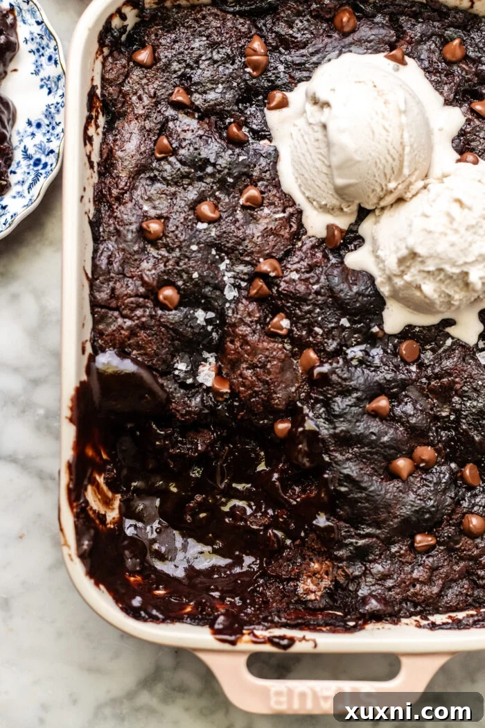 A serving of warm self-saucing chocolate pudding cake being scooped from the casserole dish, revealing the rich sauce underneath, ready to be enjoyed with ice cream.