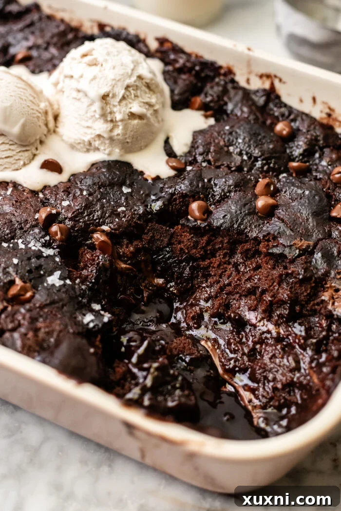 A serving of the brown butter self-saucing chocolate pudding cake, with a scoop removed, showcasing the rich chocolate sauce and cake layers.