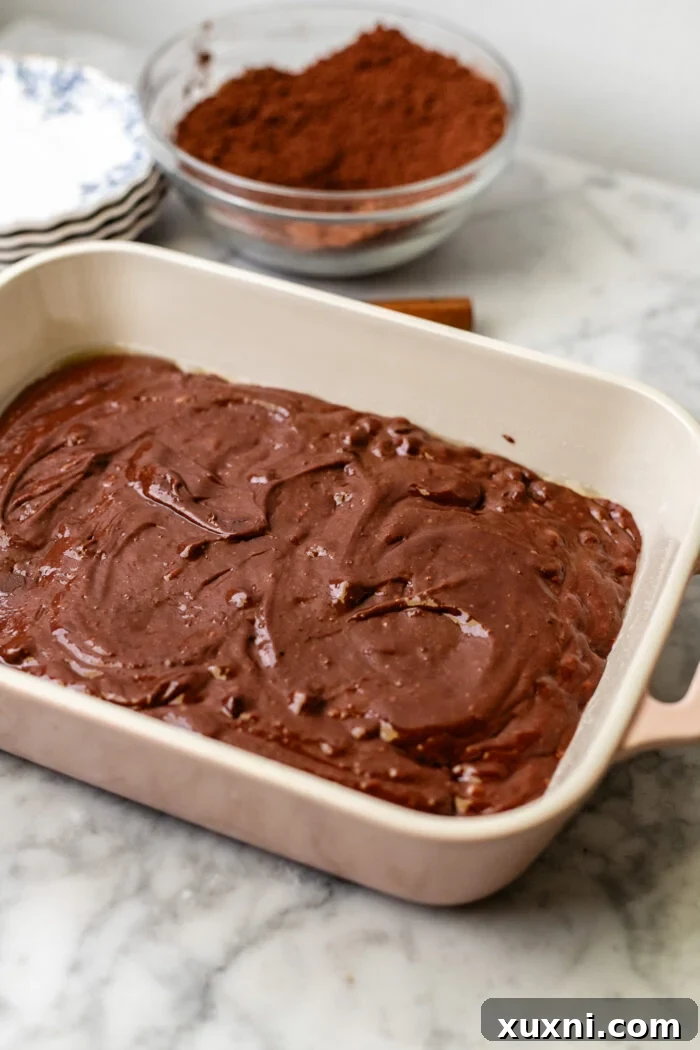Chocolate pudding cake batter being poured into a greased casserole dish, ready for baking.