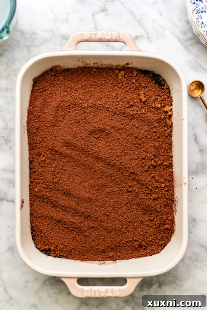 The chocolate pudding cake batter in a casserole dish, topped with the dry brown sugar and cocoa mixture, before adding water.