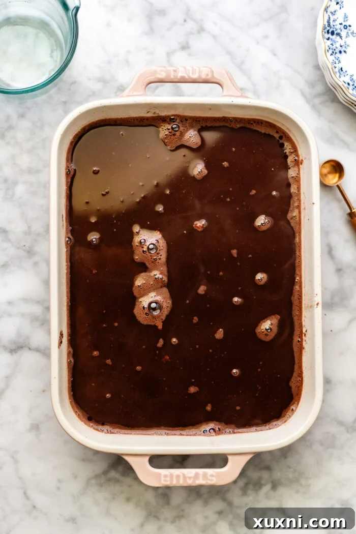 Boiling water being carefully poured over the chocolate pudding cake batter and dry topping in the casserole dish.