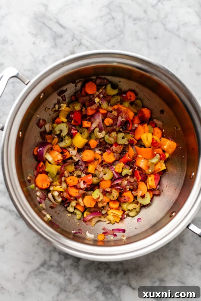 Sautéed carrots, celery, onions, and bell peppers cooking in a pot, releasing their aromas.